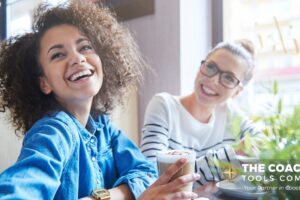 Two women smiling and sharing a coffee, symbolising gratitude, connection, and supportive relationships in coaching.